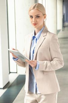オフィスの通路でタブレットを使うカメラ目線のビジネスウーマン ビジネスウーマン,ビジネス,女性の写真素材