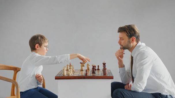 向かい合ってチェスをしている親子(グレー背景) 向かい合ってチェスをしている親子(グレー背景) チェス,親子,お父さんの写真素材