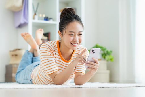 リビングでスマホを使う若い女性 リビングでスマホを使う若い女性の写真