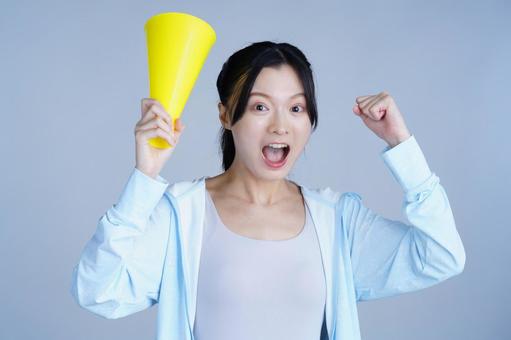 水色の服の女性が黄色いメガホンを持ち応援するの写真