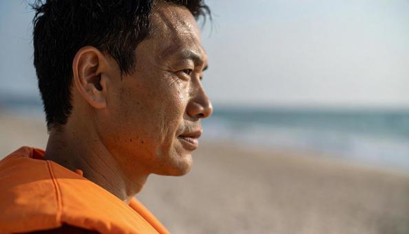 砂浜から海を見つめるライフセーバーの男性 砂浜から海を見つめるライフセーバーの男性の写真