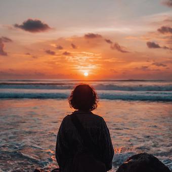 夕日に向かって海を眺める男性の後ろ姿 夕日に向かって海を眺める男性の後ろ姿の写真