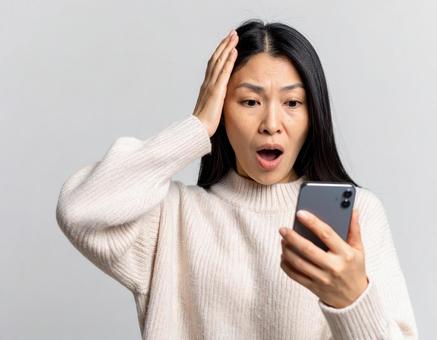 スマホを見て驚いた表情の女性 スマホを見て驚いた表情の女性の写真