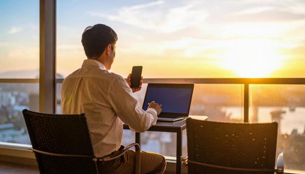 スマホを持ちながらPC作業をする男性 スマホを持ちながらPC作業をする男性の写真