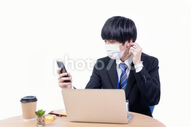 スマホを片手にマスクをかけ直す若い日本人ビジネスマン マスク,健康,ヘルスケアの写真素材