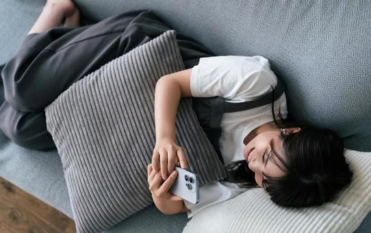 ソファに寝転んでスマホを使う女性 ソファに寝転んでスマホを使う女性 女性,スマホ,スマートフォンの写真素材