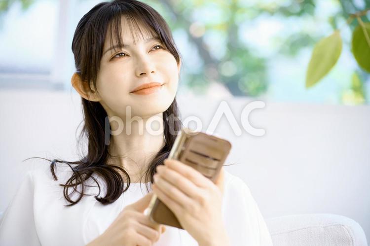 スマホを持つ若い女性　外を見る　リビング スマホ,女性,主婦の写真素材