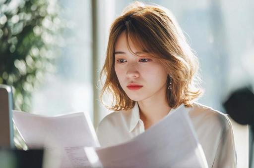 資料を見て悩むビジネス女性 資料を見て悩むビジネス女性の写真