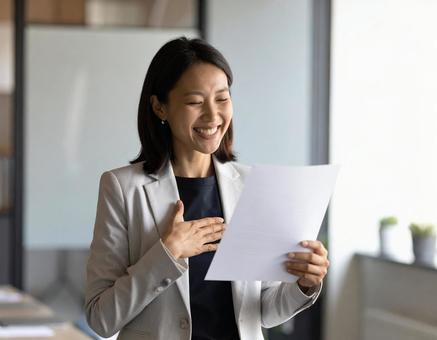 書類を見て笑顔を見せる女性社員 書類を見て笑顔を見せる女性社員の写真