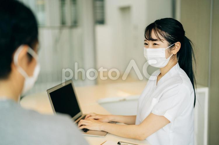 病院の受付にいる女性（マスク・患者・パソコン） 医療事務,電子カルテ,受付の写真素材