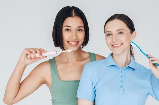 カメラ目線で仲良しで歯ブラシする女性たち カメラ目線で仲良しで歯ブラシする女性たちの写真