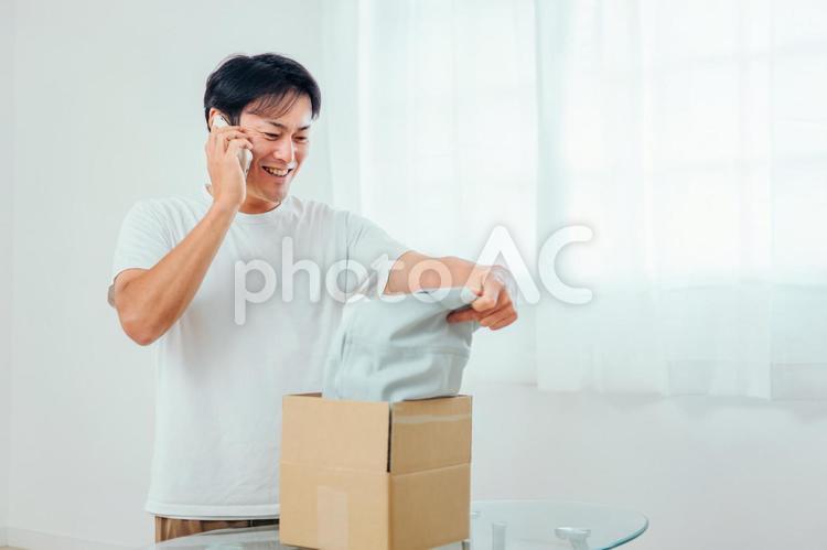 送られてきた洋服を見て電話する男性（笑顔） ギフト,宅急便,宅配便の写真素材