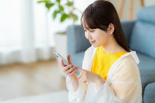 部屋でスマホを操作する若い女性 部屋でスマホを操作する若い女性 スマホ,若い女性,笑顔の写真素材