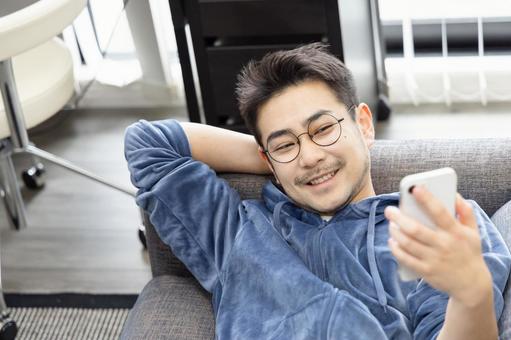ソファーで寝ながらスマホを使う男性 ソファーで寝ながらスマホを使う男性 男性,人物,スマートフォンの写真素材