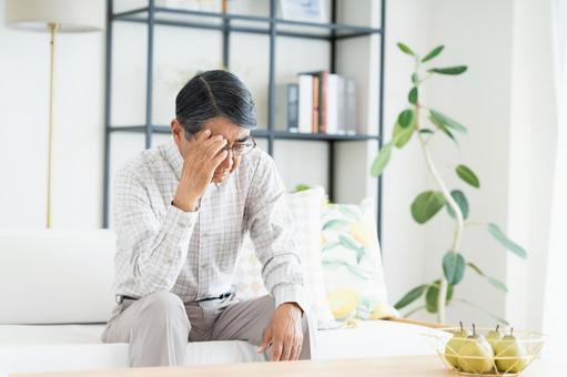 リビングで悩むシニアの男性 リビングで悩むシニアの男性の写真