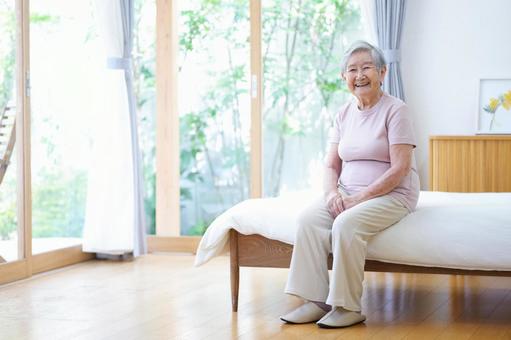 窓際のベッドに座り笑うおばあちゃん 女性,ベッド,座るの写真素材