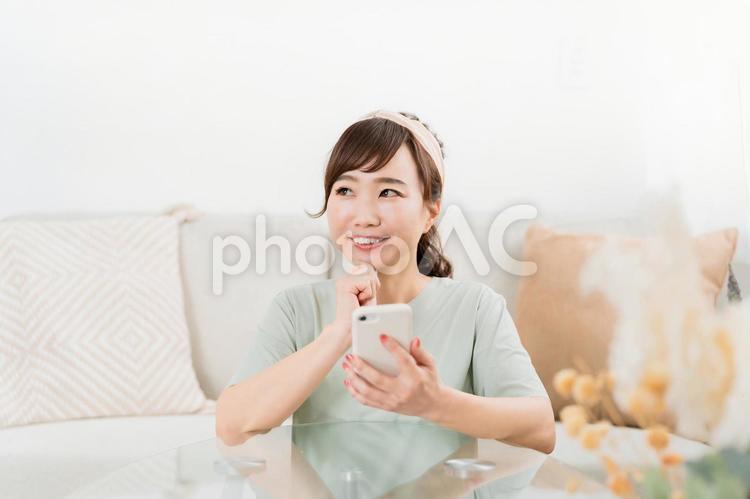 家でスマホを使う笑顔の日本人女性（迷う） スマホ,考える,迷うの写真素材