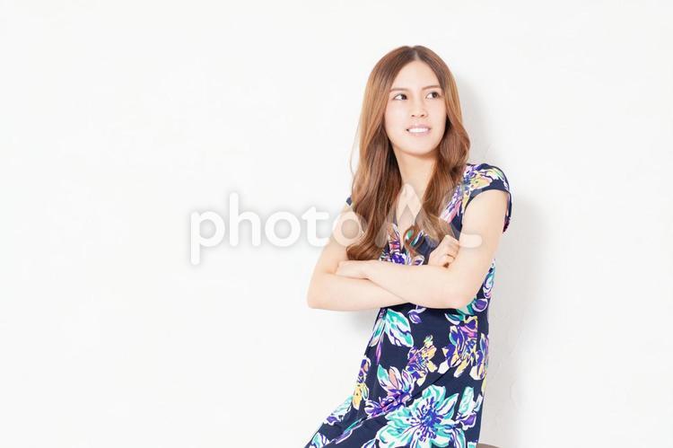 白い壁の前で腕を組んでいる、青いワンピースを着た若い女性 女性,笑う,ポーズの写真素材