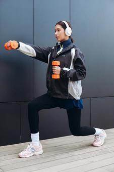 ダンベルを持って筋トレしながら足も伸ばす女性 ダンベルを持って筋トレしながら足も伸ばす女性 女性,ヘッドフォン,人物の写真素材