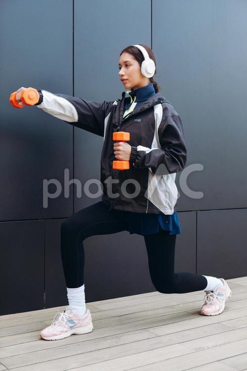 ダンベルを持って筋トレしながら足も伸ばす女性 女性,ヘッドフォン,人物の写真素材