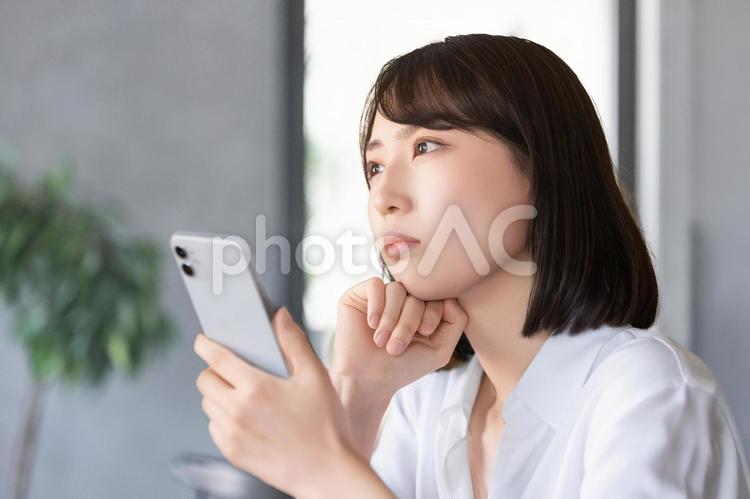 スマホを持って考えごとをする女性 女性,スマホ,考えるの写真素材