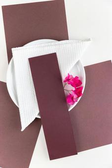 敷かれた茶色い紙と白いお皿に添えられたピンクの花と茶色いカード(白背景) 敷かれた茶色い紙と白いお皿に添えられたピンクの花と茶色いカード(白背景) モックアップ,物撮り,テーブルコーディネートの写真素材