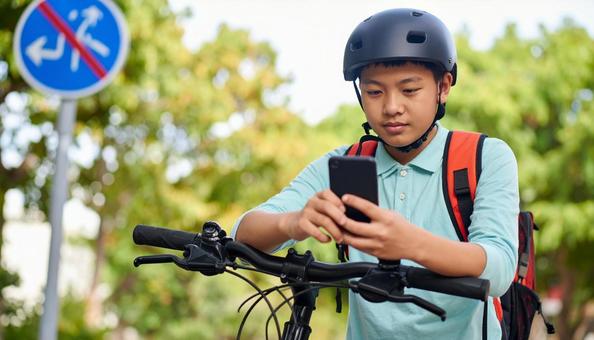 自転車を止めてスマホを見る男の子 自転車を止めてスマホを見る男の子の写真