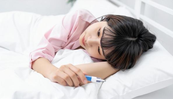 発熱して寝込んで体温計を見る女の子 発熱して寝込んで体温計を見る女の子の写真