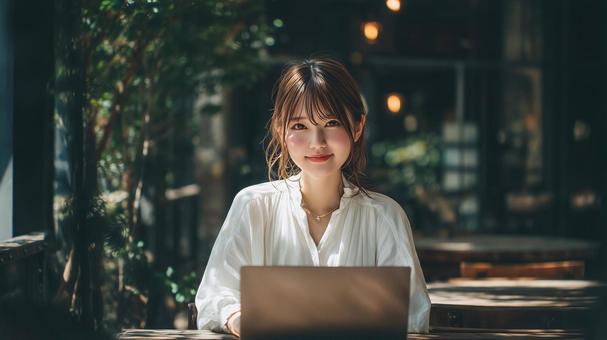 緑豊かなカフェでノートPCを使用する女性の写真