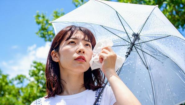 日傘をさして白いハンカチで汗を拭く女性 日傘をさして白いハンカチで汗を拭く女性の写真