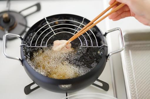 菜箸で唐揚げを揚げる手もとの写真
