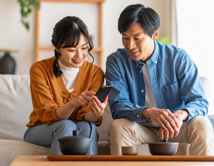 自宅のリビングでスマホを一緒に見る夫婦 自宅のリビングでスマホを一緒に見る夫婦の写真