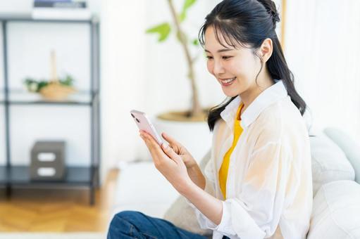 部屋でスマホを操作する女性 部屋でスマホを操作する女性 スマホ,笑顔,部屋の写真素材