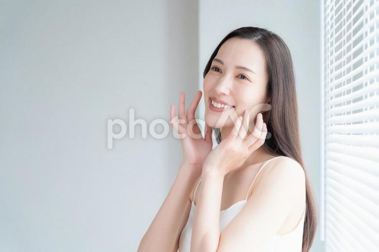 窓際でスキンケアをする若い女性 ビューティー,女性,スキンケアの写真素材