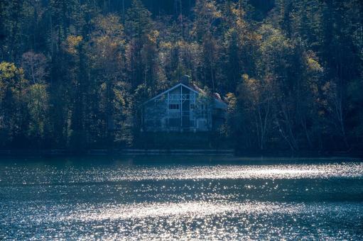 湖面に光がきらめく、静かな森に佇む建物の写真