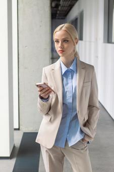 オフィスの通路でスマートフォンを持って立っているビジネスウーマン ビジネスウーマン,ビジネス,女性の写真素材