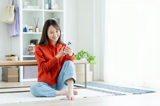 リビングでスマホを見る若い女性 スマホ,女性,笑顔の写真素材