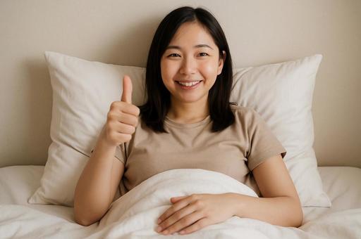 ベッドでサムズアップする女性 ベッドでサムズアップする女性の写真