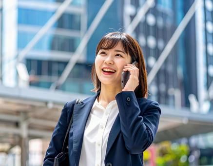 街中で電話をかける若い女性社員 街中で電話をかける若い女性社員の写真