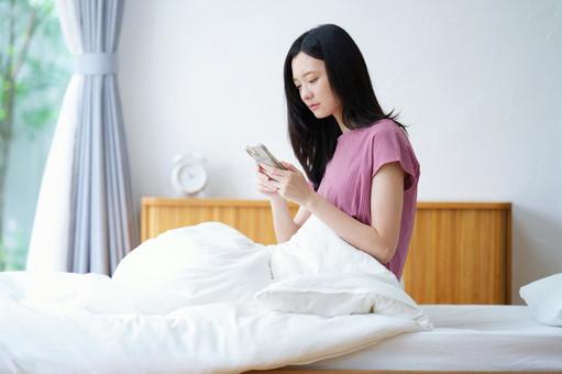真顔でベッドでスマホを見る女性 女性,スマートフォン,持つの写真素材