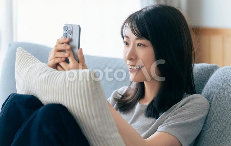 ソファに座ってスマホを使う笑顔の女性 女性,スマホ,スマートフォンの写真素材