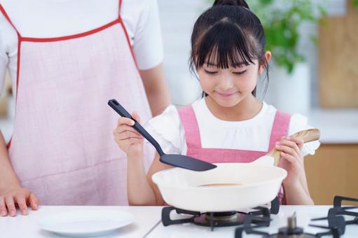 フライパンでパンケーキを焼くエプロン姿の女の子 女の子,料理,フライパンの写真素材