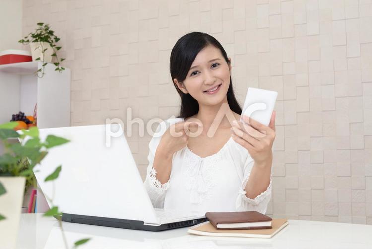 スマホを持ってパソコン作業をする女性 女性,スマホ,ビジネスの写真素材