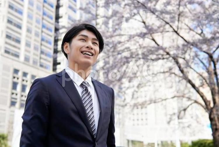 桜を背景に笑顔で立つビジネスマン	 ビジネスマン,男性,新入社員の写真素材