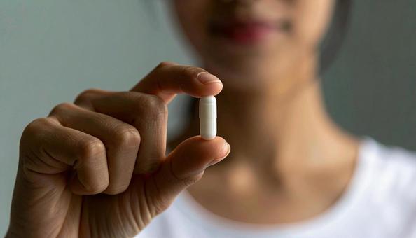 薬一錠を親指と人差し指で持つ女性 薬一錠を親指と人差し指で持つ女性の写真