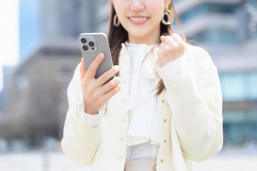 ビル街でスマホを見て喜ぶ女性 ビル街でスマホを見て喜ぶ女性 スマホ,ガッツポーズ,元気の写真素材