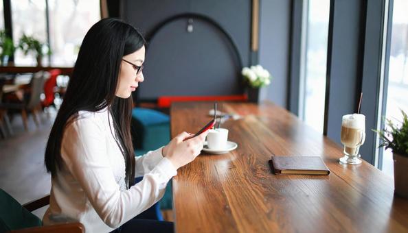 カフェで若い女性が携帯電話を見つめている カフェで若い女性が携帯電話を見つめているの写真