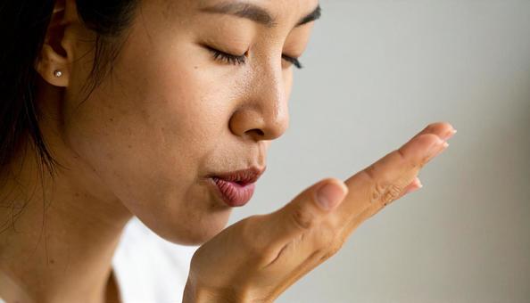 手の平に息を吹きかける女性の写真