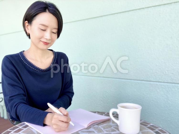 カフェテラスで日記を書く日本人女性 女性,笑顔,インタビューの写真素材