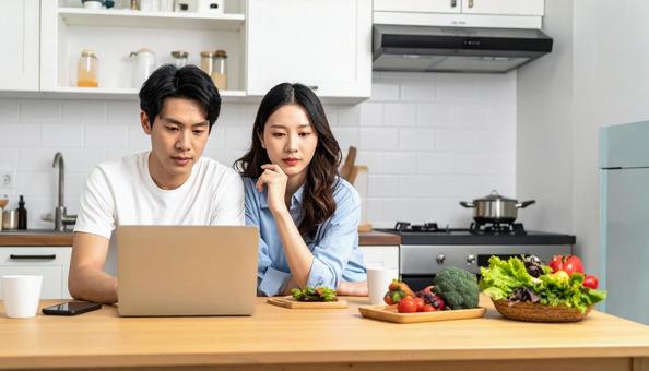 キッチンでパソコンを使い悩んでいる男女の写真